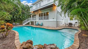 A two-story house with a swimming pool, surrounded by tropical vegetation.