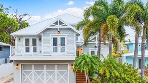 A two-story house with a garage, a balcony, and a well-maintained garden with palm trees and shrubs.