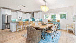 A modern kitchen with white cabinetry, a stainless steel refrigerator, a central island with bar stools, and a hanging light fixture.