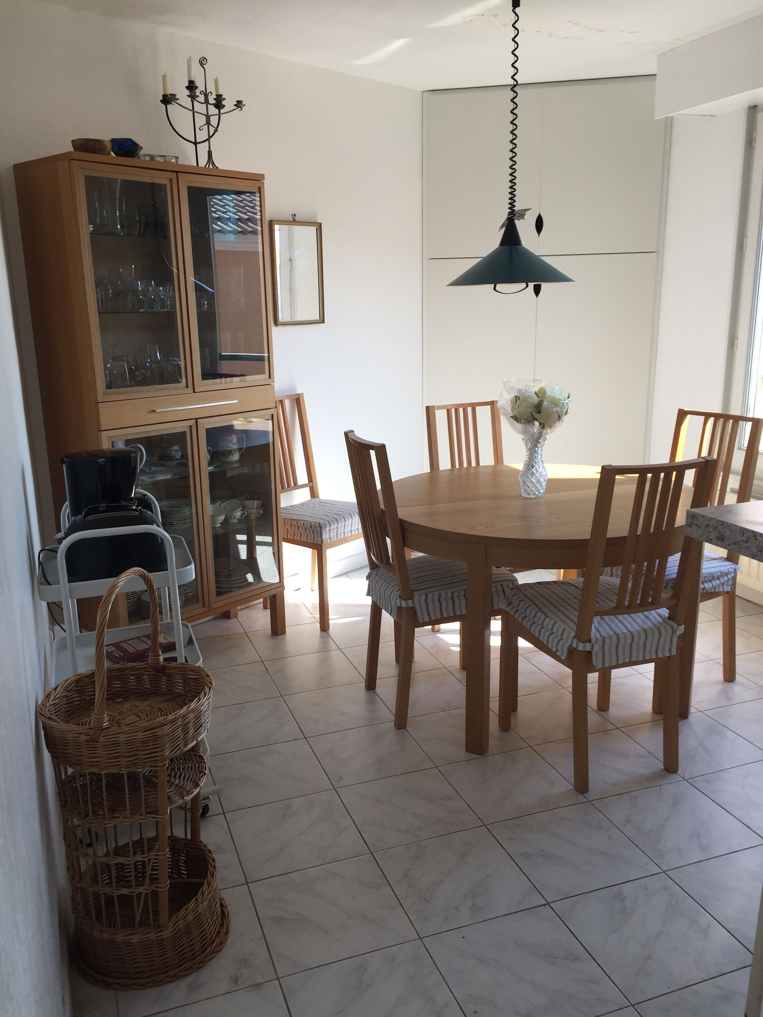 Un comedor con una mesa redonda de madera, seis sillas, una lámpara colgante y un aparador con puertas de vidrio.