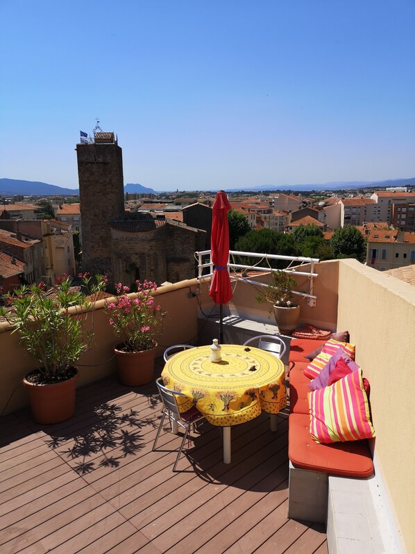 A rooftop terrace with a table, chairs, and potted plants.