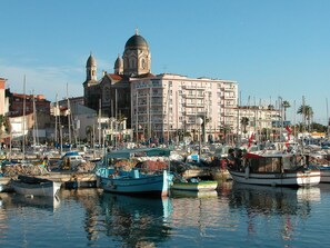 A marina with boats docked, a prominent building with domes in the background, and a clear sky.