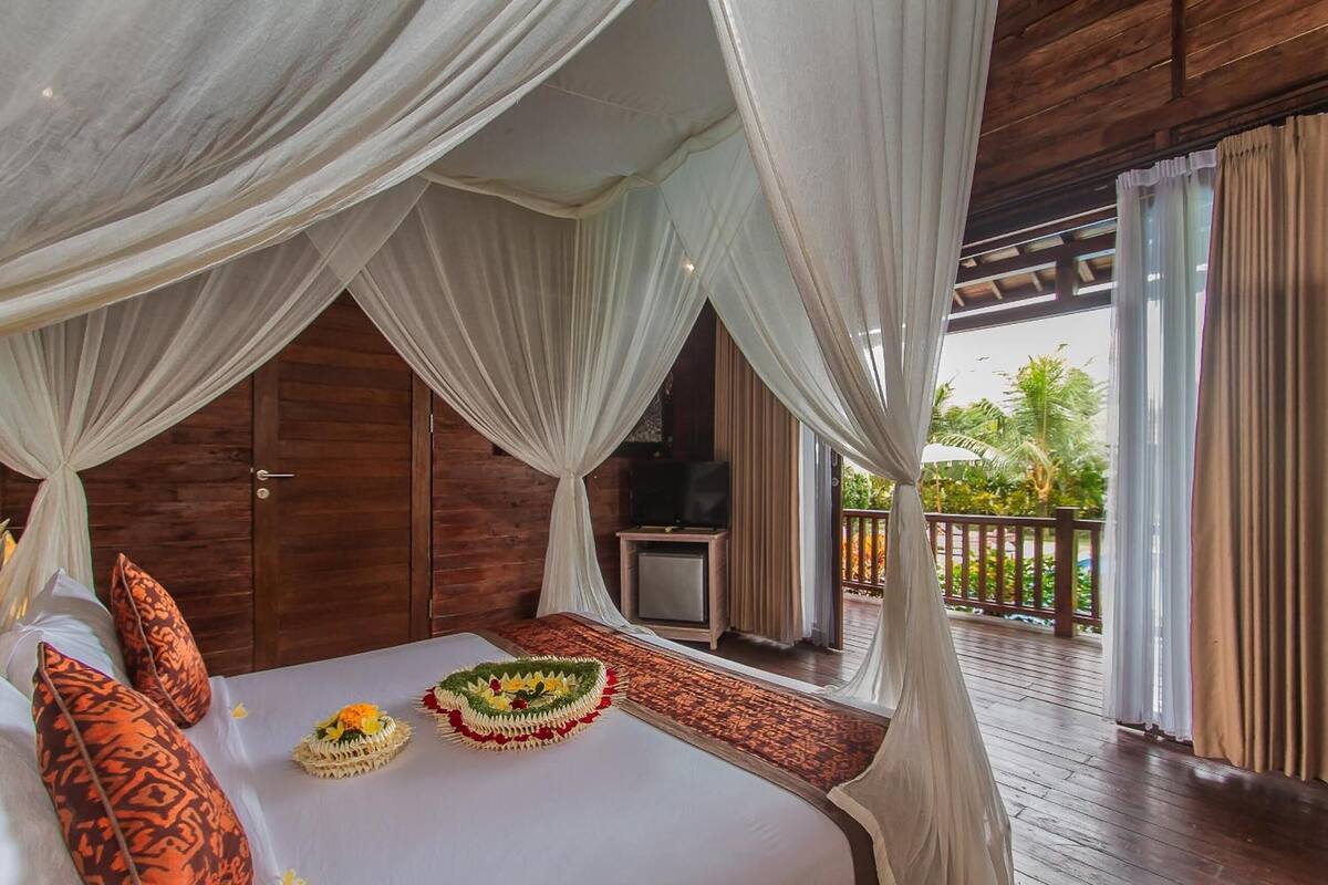 A bedroom with a bed, white canopy, patterned pillows, and a decorative floral arrangement.