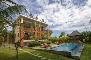 A modern two-story building with a swimming pool, surrounded by lush greenery and palm trees. - Buah Nagasari Cottages by Supala Hospitality (Ubud)