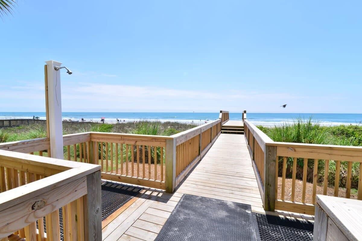 A wooden boardwalk leading to a beach with a clear view of the ocean.