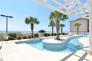 Une piscine au design incurvé, entourée de palmiers et agrémentée d’une pergola blanche.
