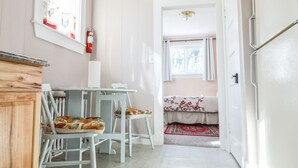 Une pièce chaleureuse avec un meuble en bois, une table blanche avec des chaises, une fenêtre avec des rideaux et un lit recouvert d’une couvre-lit à motifs.