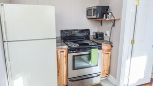 Une cuisine compacte équipée d’un réfrigérateur, d’une cuisinière, d’un four, d’un four à micro-ondes et d’une petite étagère au-dessus de la cuisinière.