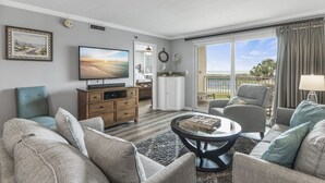 A living room with a TV, sofas, a coffee table, and a view of the outdoors. - 🌅Islander #204 Luxury Living with Sunrise Views & Gulf Wildlife Watching🌊🐬 (Destin)