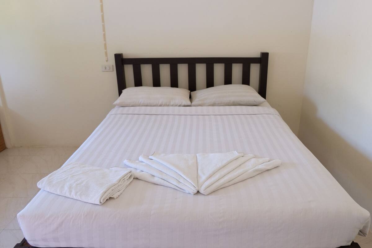A single bed with white bedding and pillows, a wooden headboard, and a neatly folded towel on the bed.