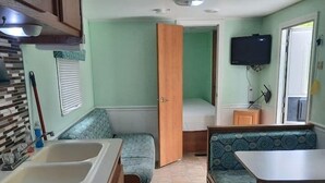 Ein kompaktes Wohnmobil-Interieur mit einer Küchenzeile, einem kleinen Bett, einer Sitzecke und einem Fernseher.