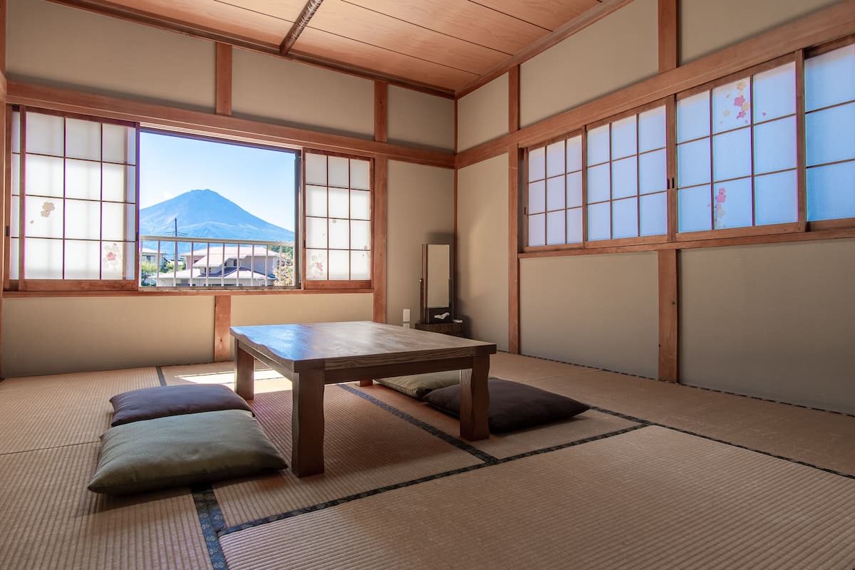A tatami mat room with a low table and cushions, large windows with a view of a mountain, and traditional wooden beams.