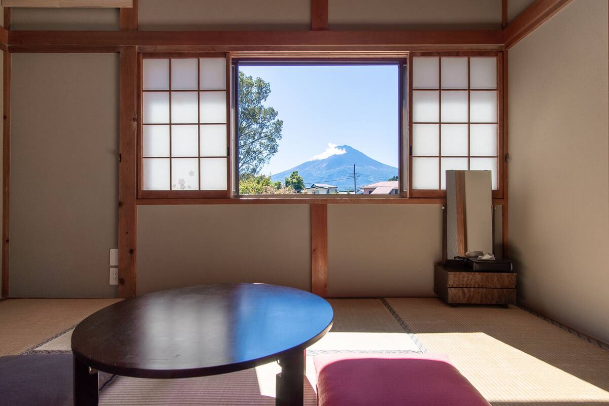 A traditional Japanese room with tatami flooring, a sliding shoji screen, a wooden table, and a view of a mountain.