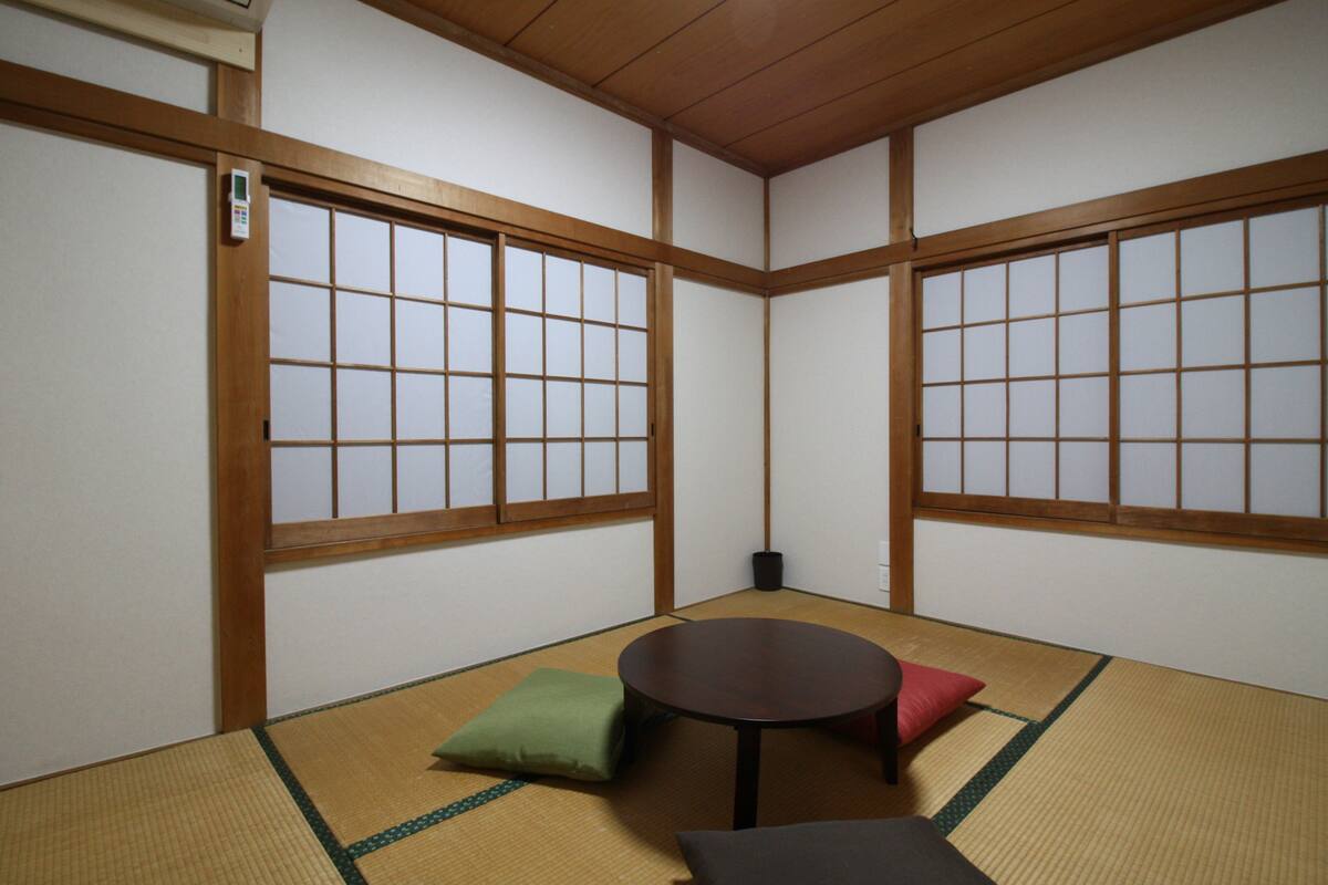 A tatami room with a low wooden table, green and black cushions, and shoji screens.