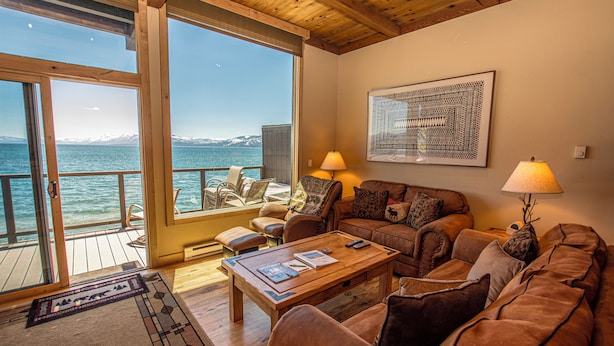Uma sala de estar acolhedora com piso de madeira, sofá, mesa de centro e vista para o mar.