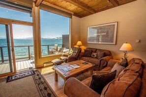 A cozy living room with a wooden floor, a sofa set, a coffee table, and a view of the sea.