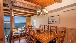 Uma área de refeições com uma mesa e cadeiras de madeira, um lustre e vista para o oceano.