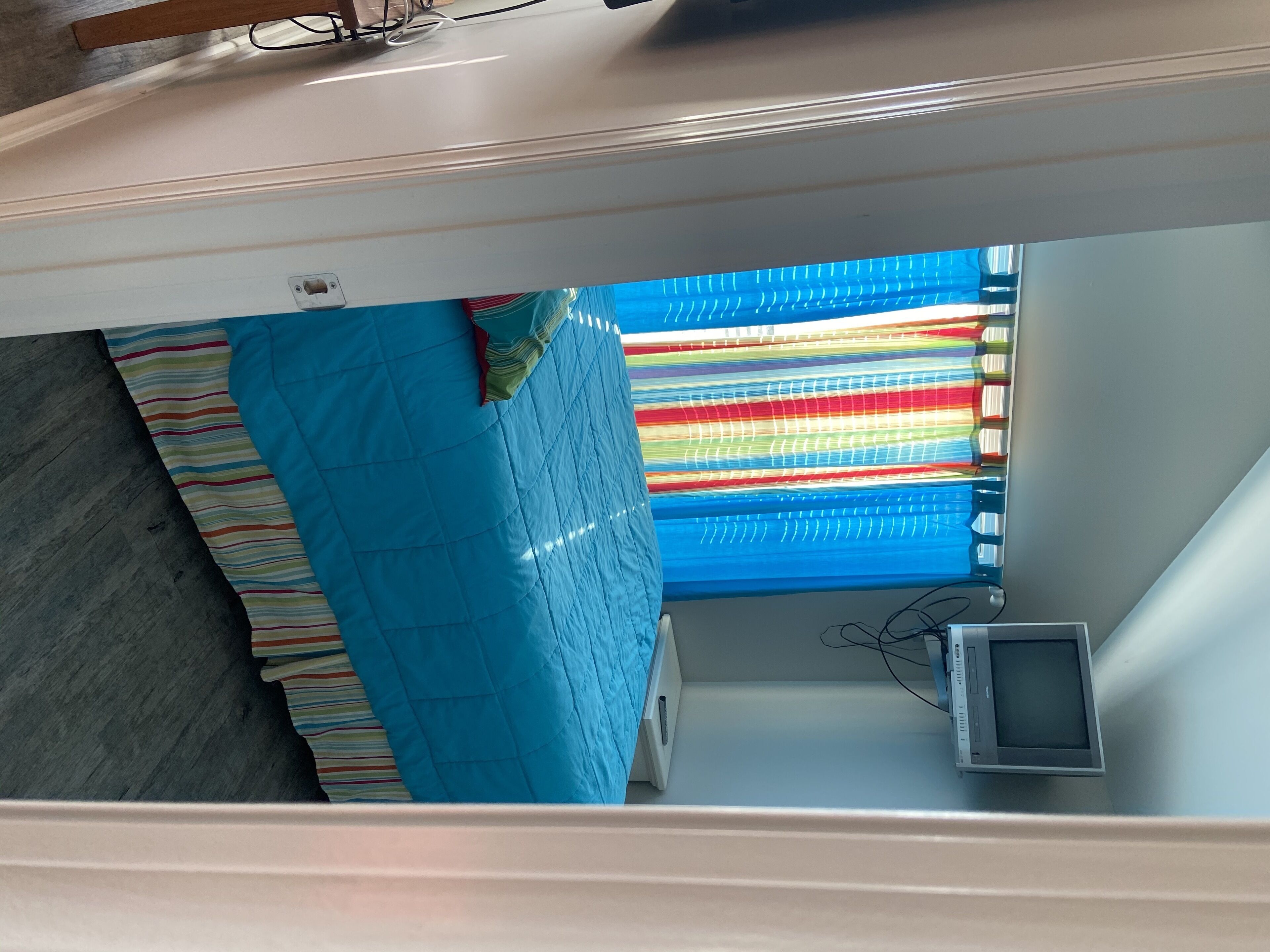 Una habitación con cama, televisión y ventana con cortinas a rayas.