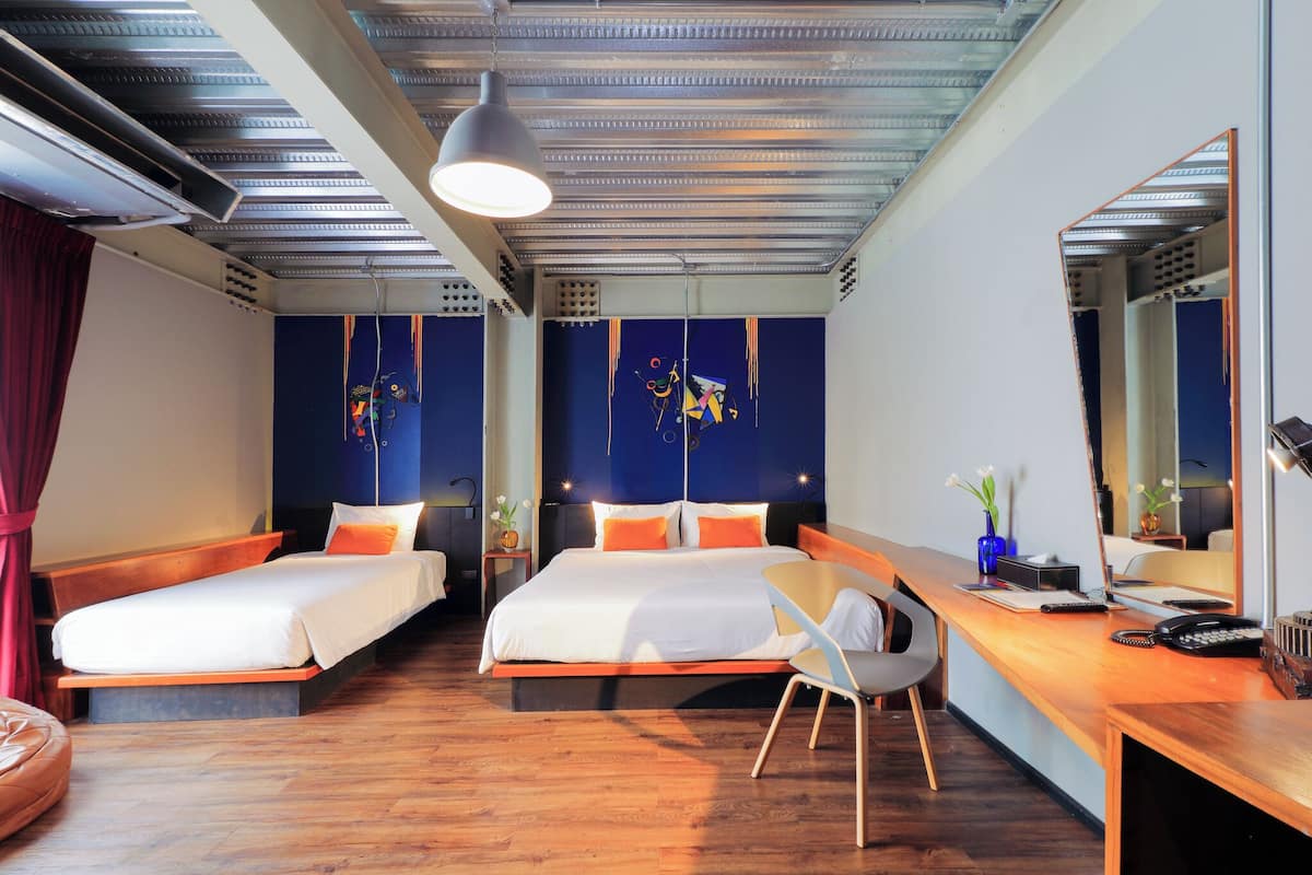 A hotel room with two single beds, a desk with a chair, a large mirror, and a ceiling fan.