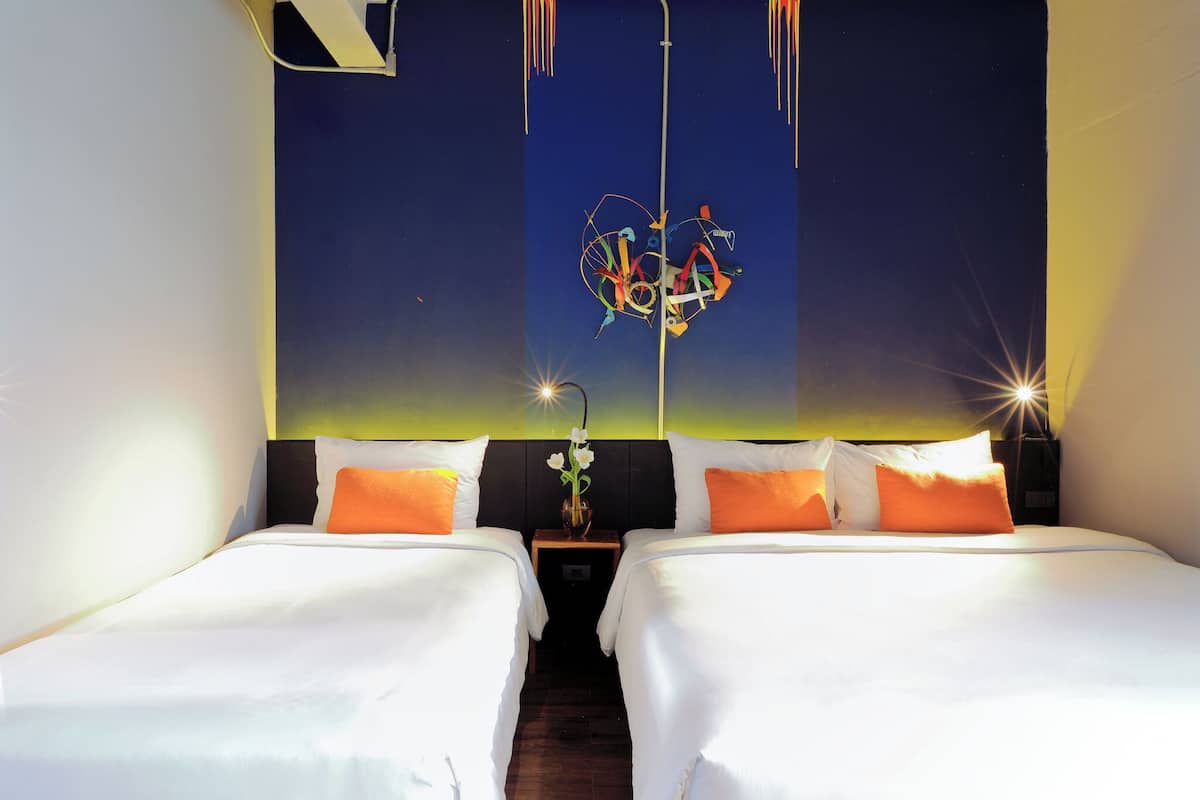 A hotel room with two beds, a nightstand, and a wall with a decorative light fixture.