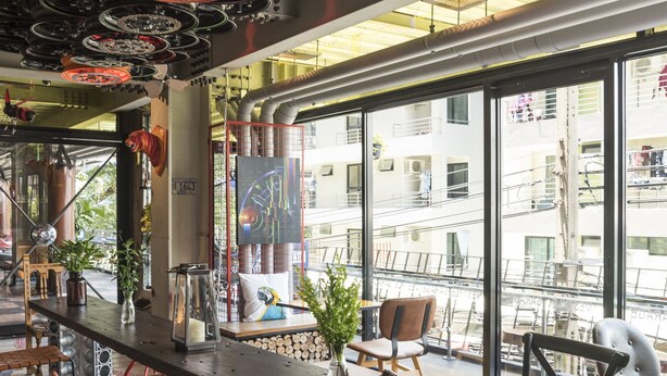 A modern interior with a long table, chairs, and large windows overlooking a cityscape. - MeStyle Garage Hotel (Bangkok)