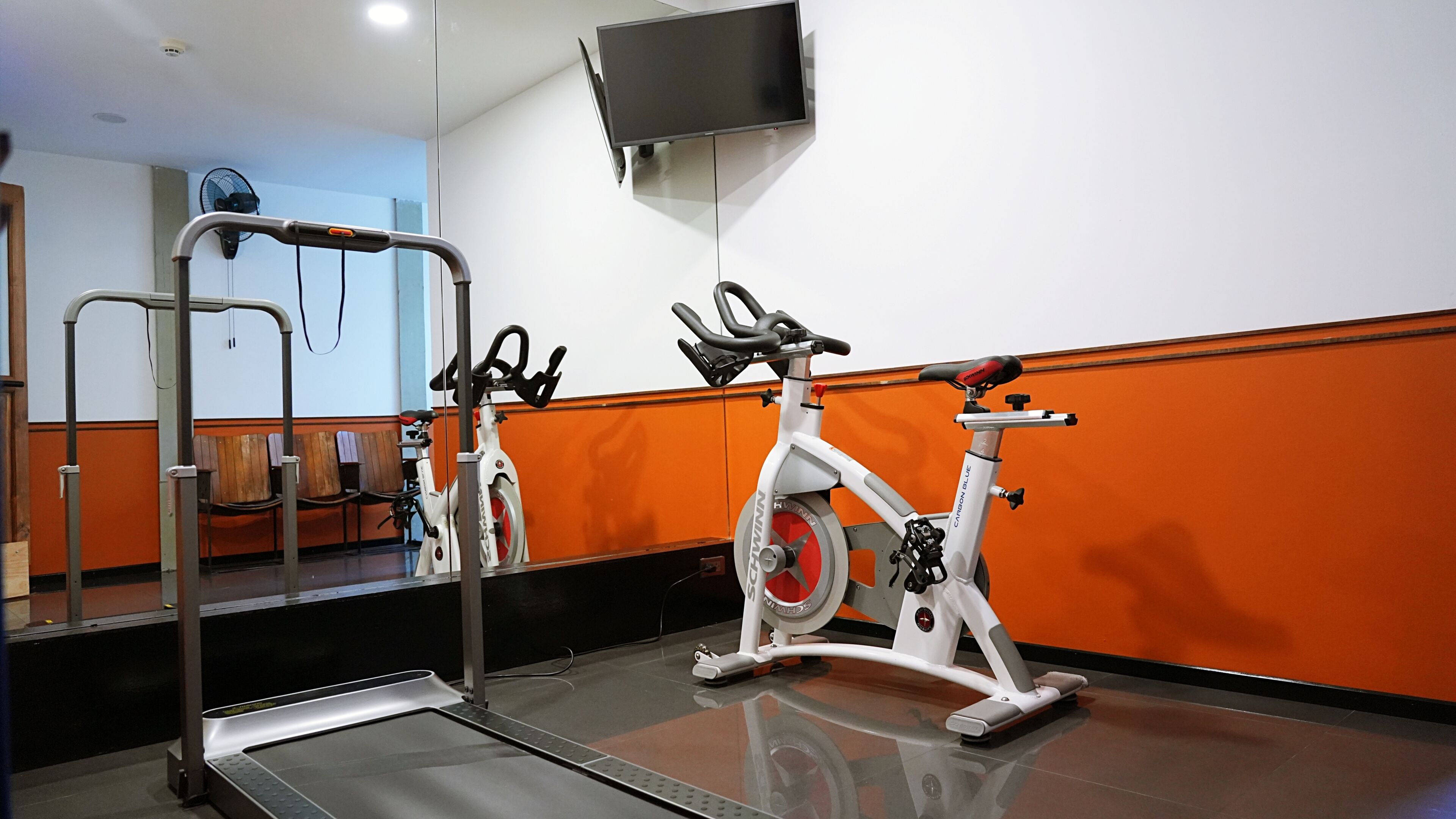 A gym with a treadmill, stationary bikes, and a mirrored wall.