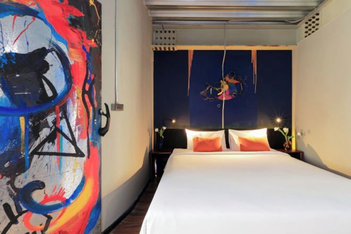 A hotel room with a large abstract painting on one wall, a bed with white linens, and a night sky view through the window.