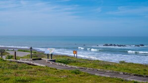 A coastal road with a wooden boardwalk, signs, and a view of the ocean. - Beautiful Moonstone Beach Rental Just Steps Away From the Boardwalk! (Cambria)