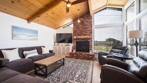 A cozy living room with a fireplace, leather sofas, a coffee table, and a large TV. - Beautiful Moonstone Beach Rental Just Steps Away From the Boardwalk! (Cambria)
