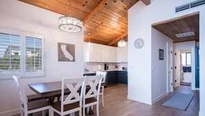 A modern kitchen with wooden beams, white cabinets, and a dining area with a wooden table and white chairs. - Beautiful Moonstone Beach Rental Just Steps Away From the Boardwalk! (Cambria)