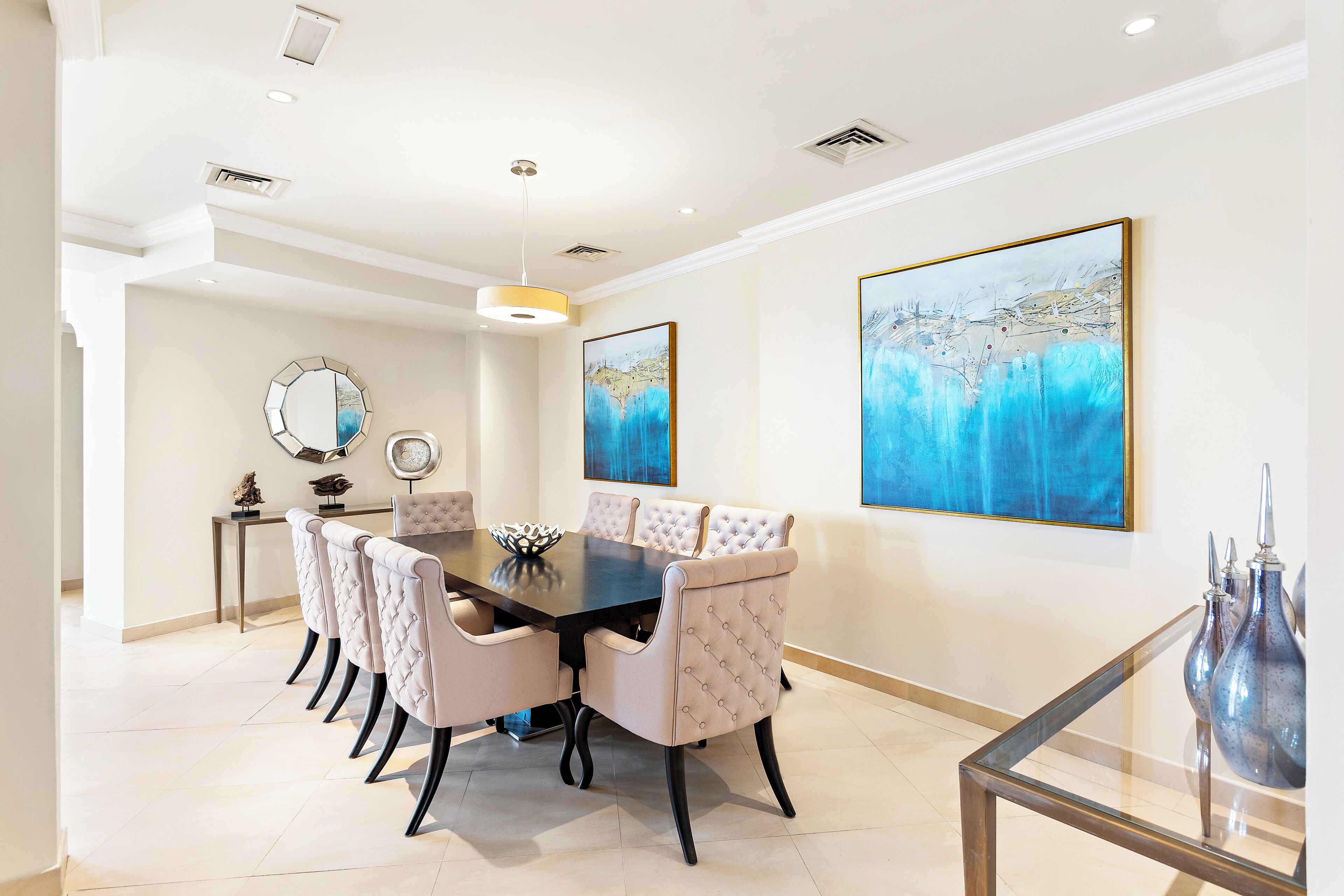 A dining area with a round table, cushioned chairs, and artwork on the walls.