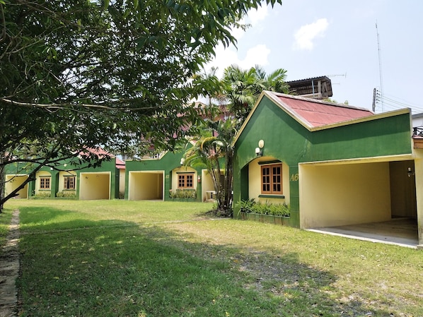 A row of green buildings with numbered doors, a tree in the foreground, and a clear sky.