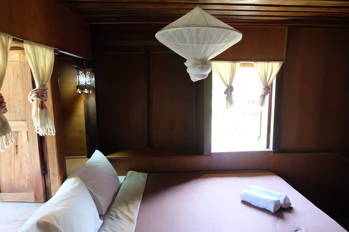 A room with a bed, a hanging mosquito net, and curtains tied back.