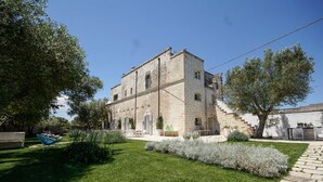 A stone building with a central courtyard, surrounded by greenery and a paved walkway. - Masseria Spartivento (Melendugno)