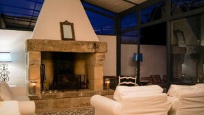 A cozy living room with a stone fireplace, white upholstered chairs, and a patterned rug. - Masseria Spartivento (Melendugno)
