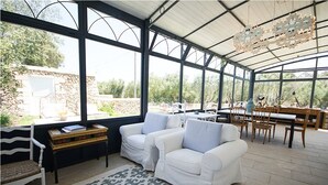 A spacious conservatory with white furniture, a patterned rug, and a dining area with wooden chairs and a table. - Masseria Spartivento (Melendugno)