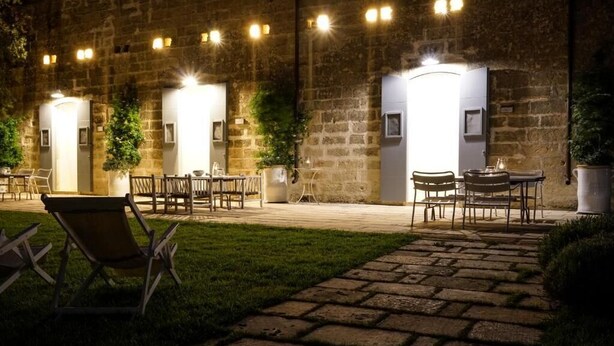 An outdoor patio area with stone flooring, wooden tables and chairs, and potted plants. - Masseria Spartivento (Melendugno)