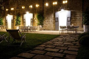 An outdoor patio area with stone flooring, wooden tables and chairs, and potted plants. - Masseria Spartivento (Melendugno)