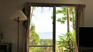 A room with a sliding glass door leading to a garden, a television on the right, and a lamp on the left. - Uminosoba Pension (Ginoza)