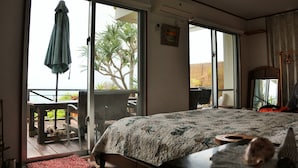 A bedroom with a large bed, a sliding glass door leading to a balcony, and a ceiling fan. - Uminosoba Pension (Ginoza)