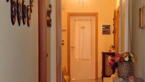 A hallway with a wooden floor, a door at the end, and a decorative cabinet with a vase of flowers. - B&B A Due Passi (Otranto)