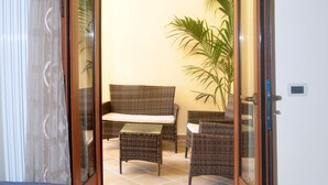 A room with a bed, a dining table, and chairs, a potted plant, and a sliding glass door leading to an outdoor area with a wicker sofa and another plant. - B&B A Due Passi (Otranto)