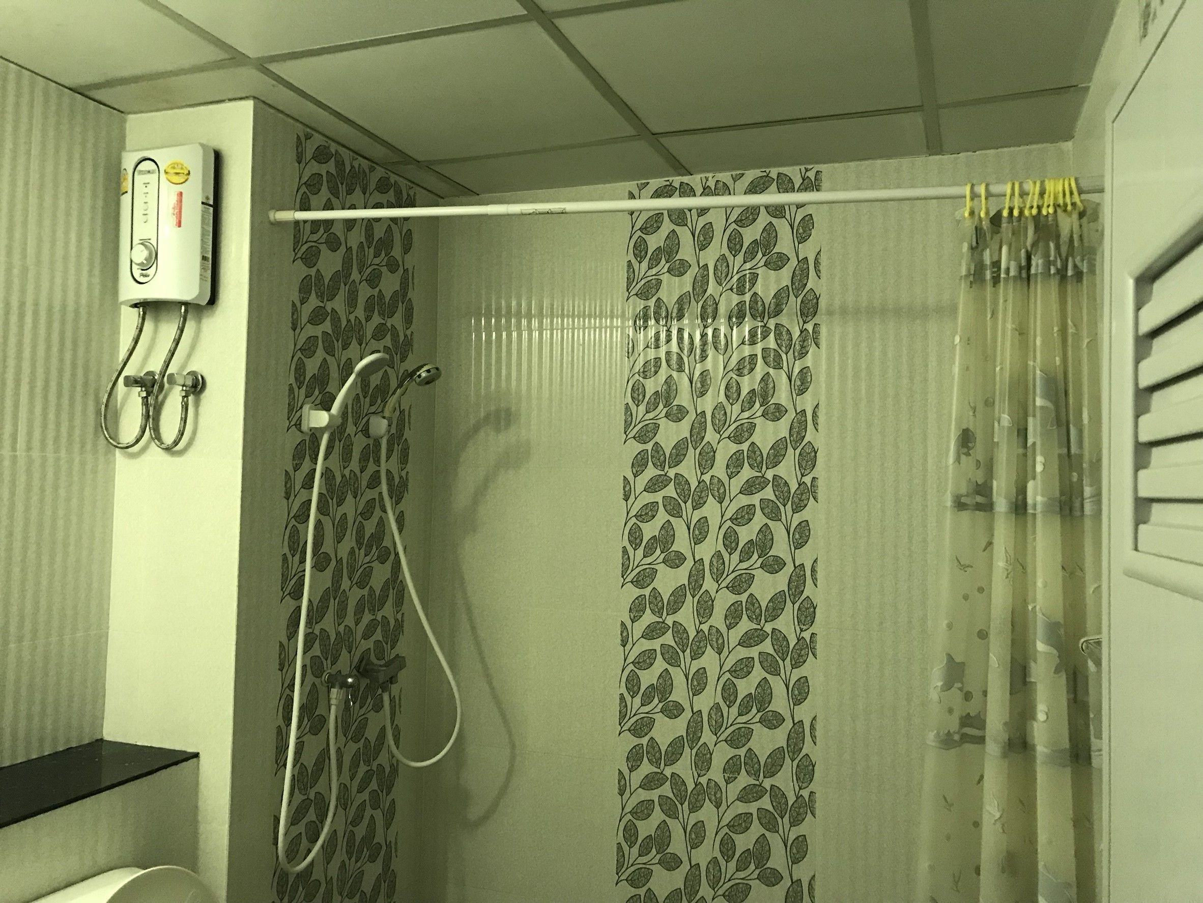 Ducha con cortina estampada con hojas, cabezal de ducha de mano y panel de control en la pared.