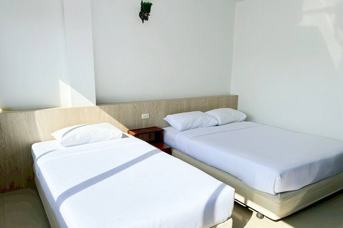 Une chambre avec deux lits, une tête de lit en bois, une table de chevet et un luminaire fixé au mur.
