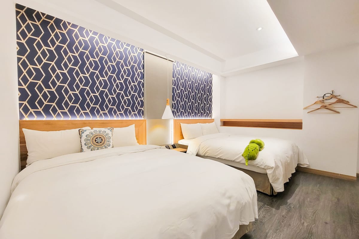 A hotel room with two beds, a wooden headboard, a geometric patterned wall, a wooden floor, and a ceiling light.