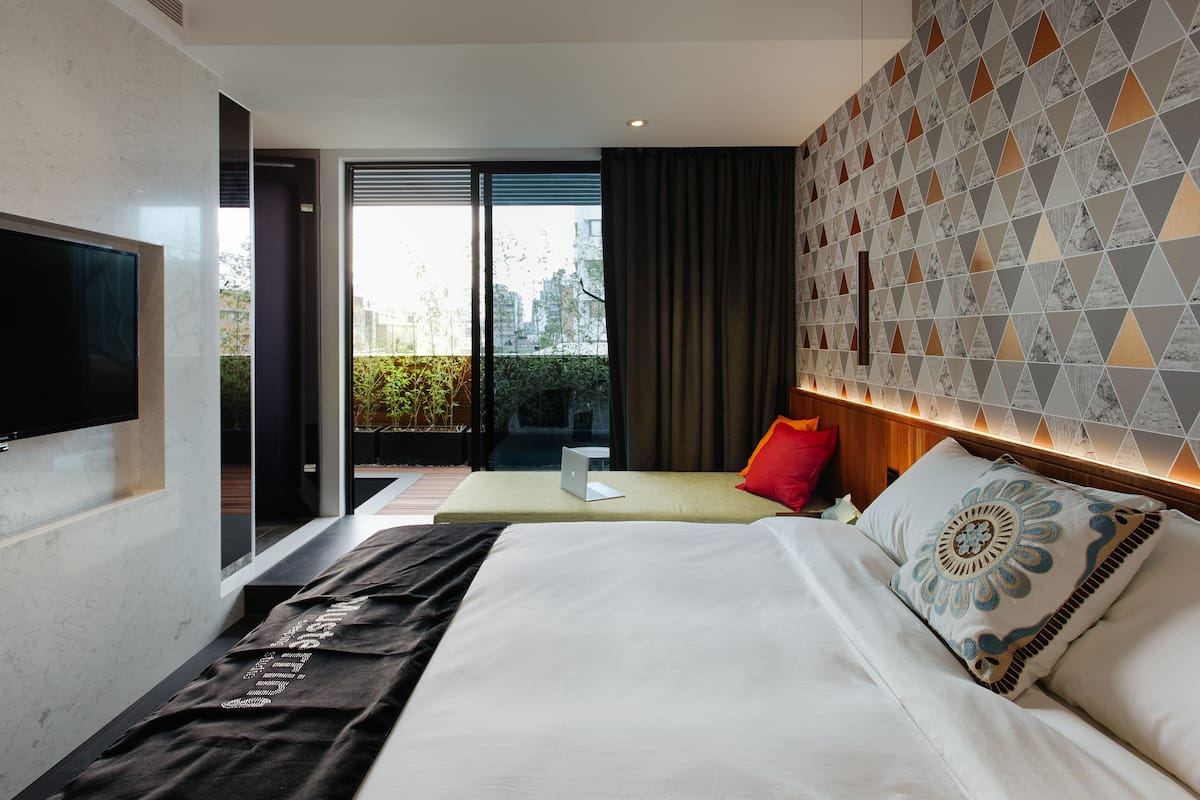 A modern hotel room with a large bed, a desk, and a TV.