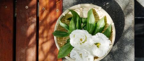 Una cesta tejida con flores blancas y hojas verdes sobre una superficie de madera.