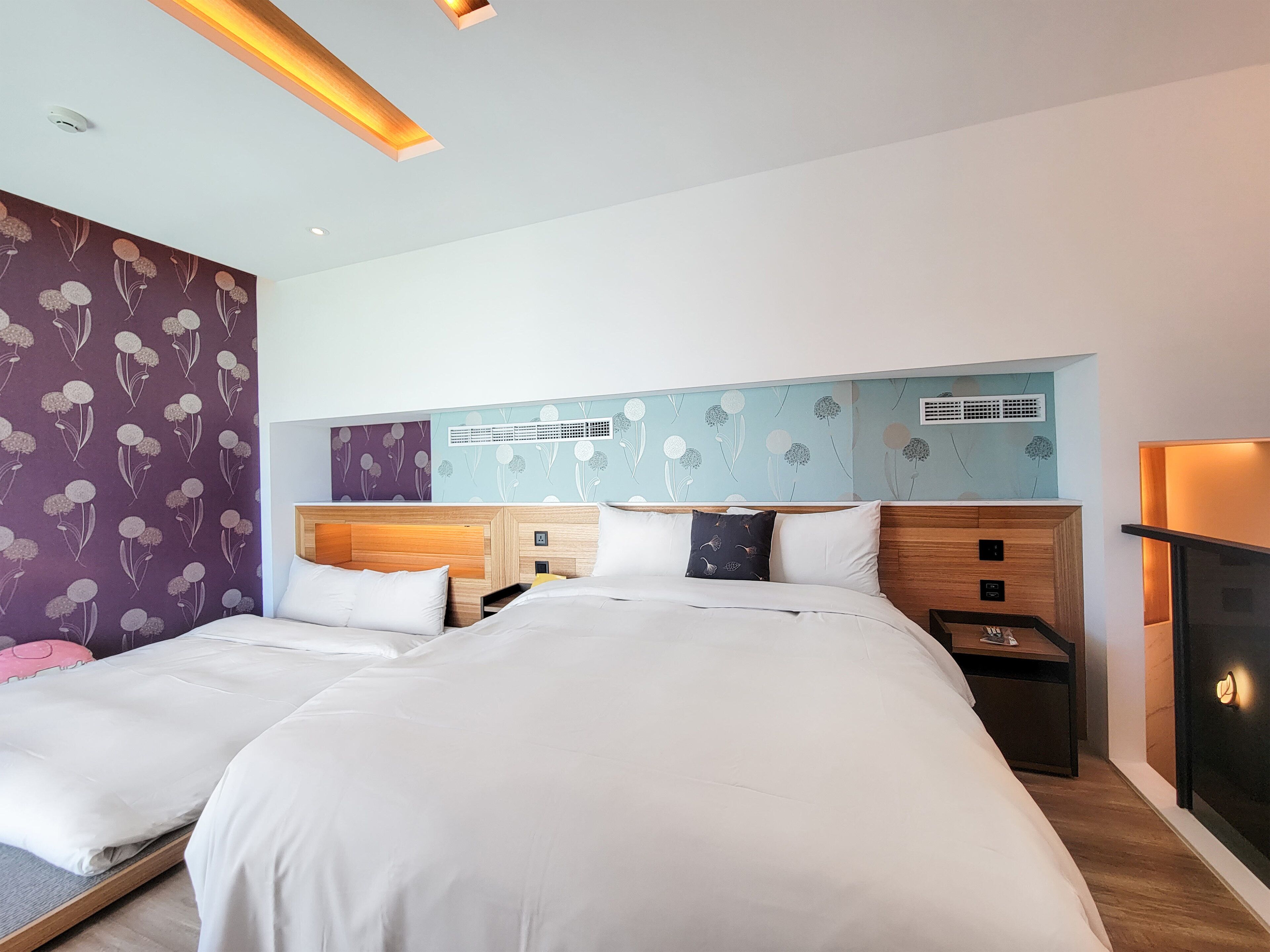 A modern hotel room with a large bed, wooden headboard, and a decorative wall with floral patterns.