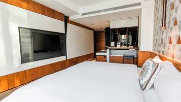 A modern hotel room with a large bed, a TV mounted on the wall, a small kitchenette, and a bathroom with a mirror.