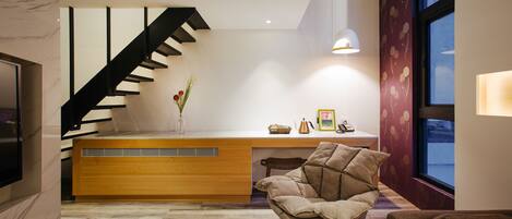 Un interior moderno con un mostrador de recepción de madera, una escalera negra, un sillón mecedora y un ventanal grande.